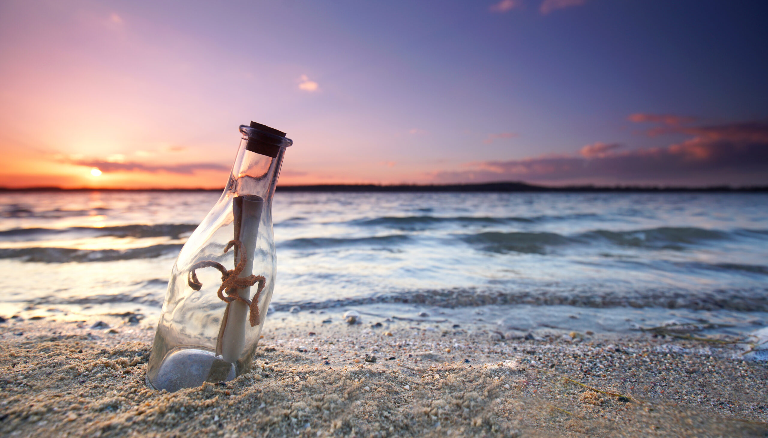 Image d'une bouteille contenant un message, échouée dans le sable d'une plage au coucher du soleil